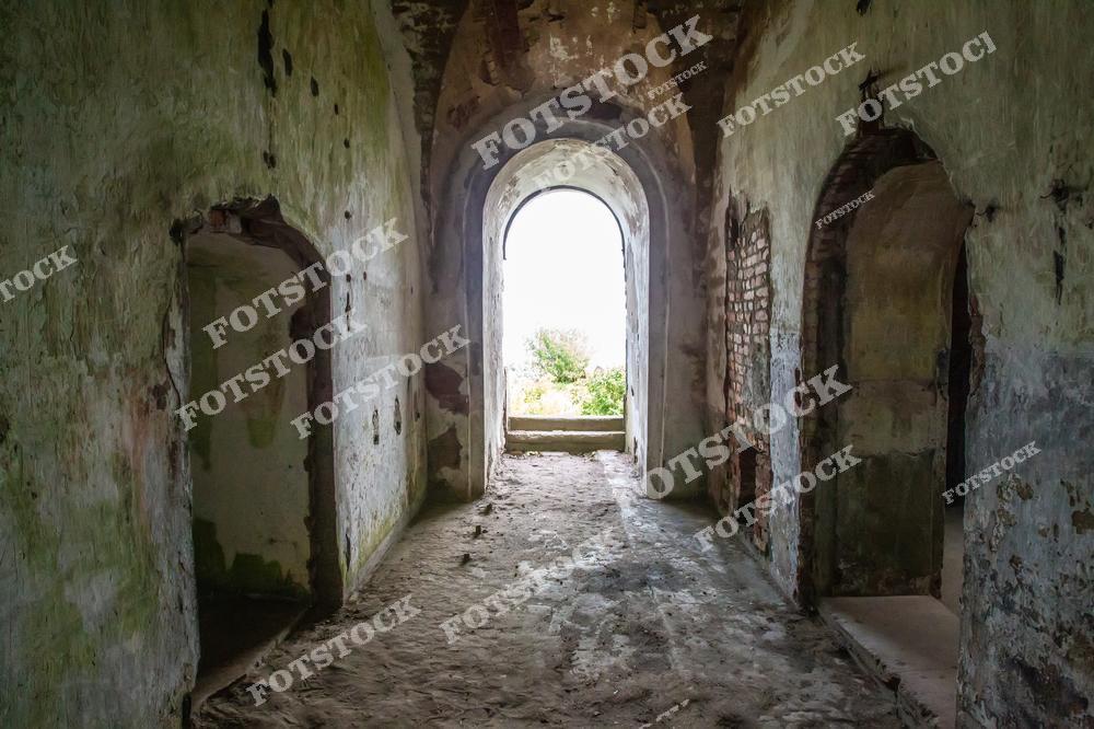 На фотографии изображен коридор старого заброшенного здания с облупившимися светло-зелеными стенами. Видны круглые дверные проемы и обшарпанные поверхности, что подчеркивает запустение и упадок этого пространства.