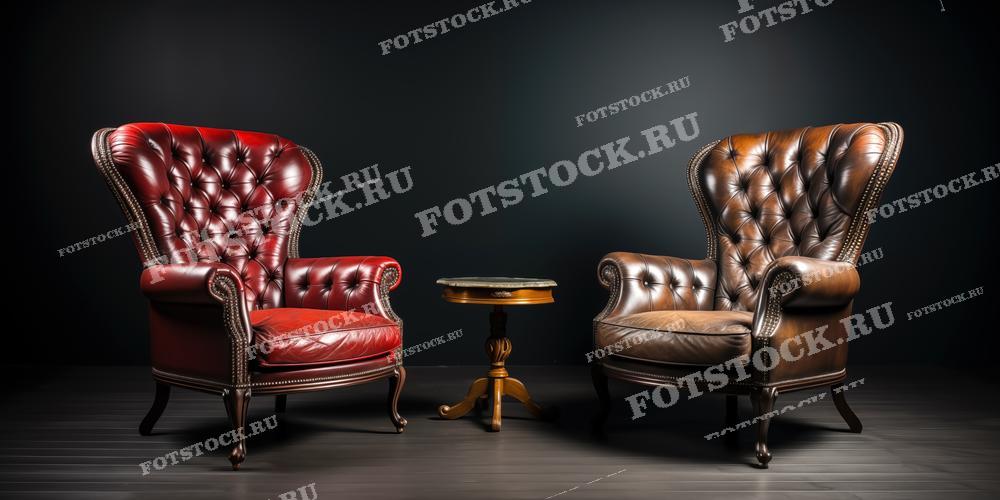 На фотографии изображены два роскошных кожаных кресла: одно красное, другое коричневое, выполненные в классическом английском стиле с элементами капитоне. Между ними расположен элегантный столик на золотистой ножке. Это изображение может быть использовано для каталогов мебели, рекламы интерьеров или веб-сайтов, специализирующихся на домашнем декоре и украшениях. Также фотография подойдет для статей о классическом дизайне интерьера и для использования в дизайне магазинов мебели.