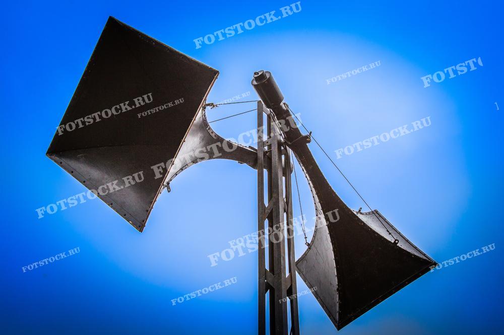 Фотография демонстрирует старые громкоговорители на синем фоне. Снимок передает атмосферу ретро технологий и напоминает о ранних системах звуковой связи.