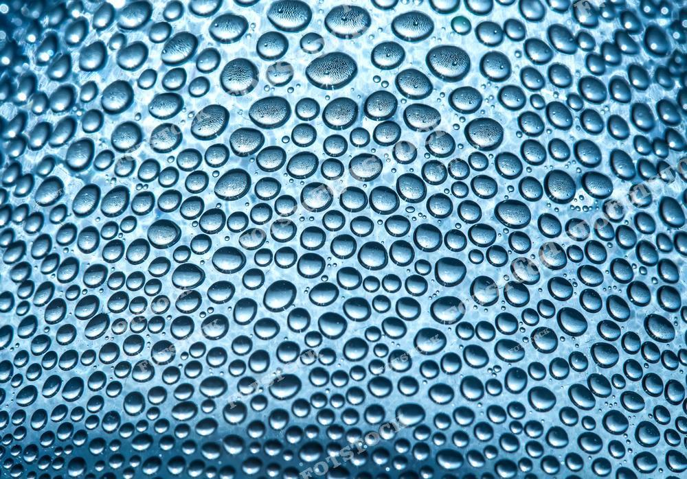 Фотография плотного узора капель воды на стеклянной поверхности, создающего интересную текстуру. Капли различного размера отражают свет, придавая изображению ощущение прохлады и свежести. Подходит для использования в качестве абстрактного фона или текстуры.