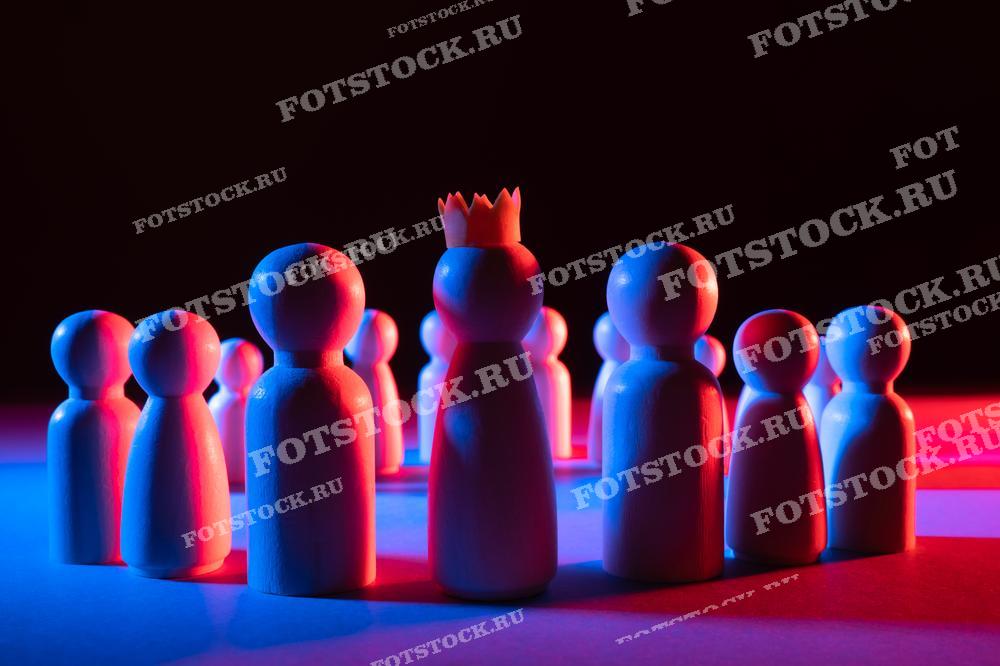Фотография показывает деревянные фигурки людей, стоящих в круге, с одной фигуркой в центре, носящей корону. Эта сцена символизирует лидерство, власть и социальную иерархию.