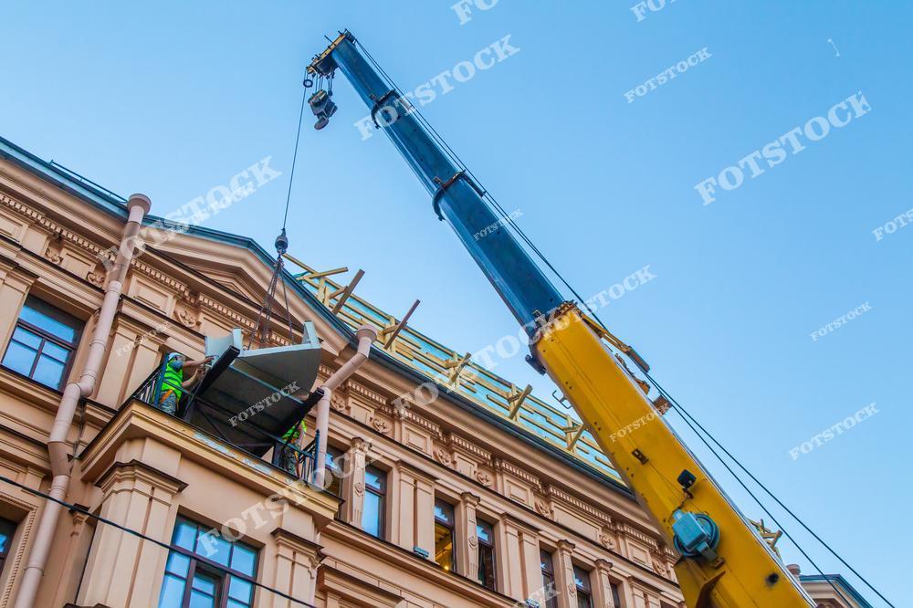 На фотографии изображён кран, поднимающий конструкцию к фасаду исторического здания. В кадре видно процесс установки или реконструкции элементов на крыше. Снимок демонстрирует сочетание современной техники и сохранения архитектурного наследия.