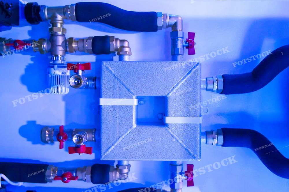 На фотографии изображена система газопроводов с различными кранами, вентилями и соединениями. В центре кадра находится узел, который кажется центральной частью системы газоснабжения. Такое изображение может использоваться для иллюстрации инженерных решений в области газоснабжения и газового отопления.