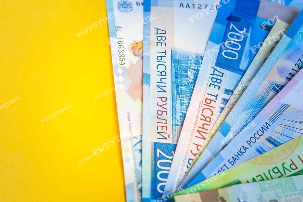 На изображении веером разложены купюры номиналом 2000 рублей на ярком желтом фоне. Композиция символизирует финансовую стабильность и денежный оборот в России.