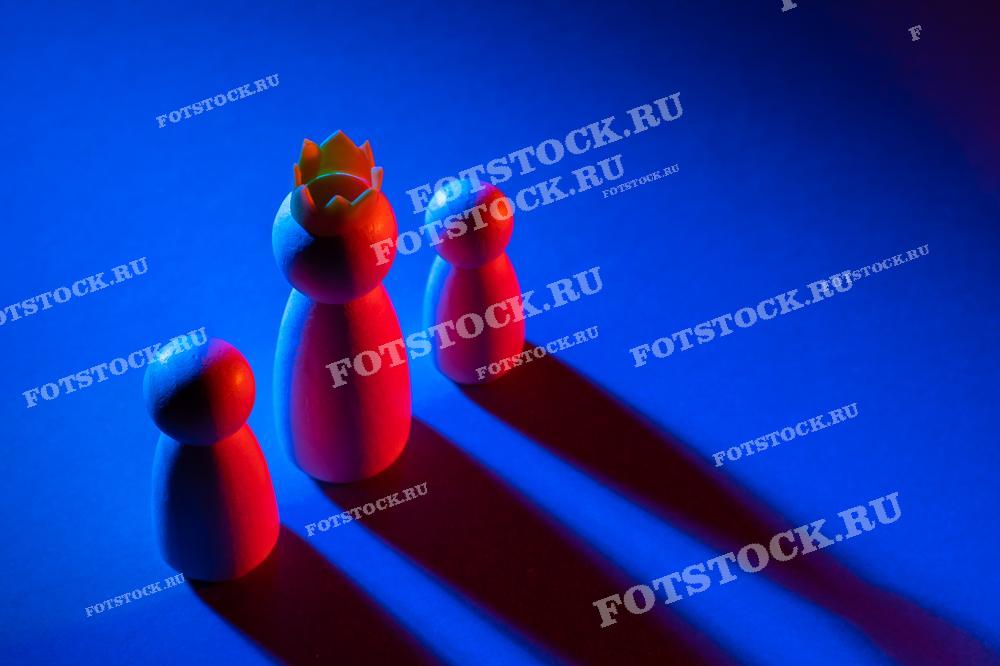 Фотография показывает три деревянные фигуры на синем фоне, одна из которых выделяется короной на голове. Это изображение символизирует лидерство, власть и иерархию.