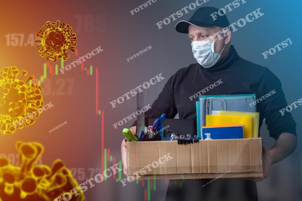 На изображении мужчина в защитной маске, держащий коробку с рабочими принадлежностями. На фоне виден график снижения и вирусные частицы, символизирующие пандемию и экономические трудности.