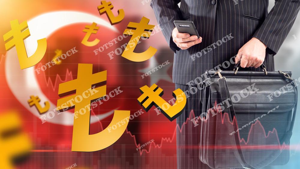 На изображении мужчина в деловом костюме держит телефон и портфель, а на фоне виден турецкий флаг, графики и символы турецкой лиры. Композиция подчеркивает нестабильность валютного рынка и влияние экономических факторов.