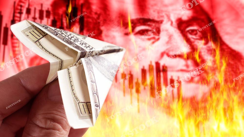 На изображении показана стодолларовая банкнота, сложенная в виде бумажного самолета, что символизирует легкость потери денег. На фоне изображены огонь, финансовый график и крупное лицо Бенджамина Франклина, что усиливает ассоциацию с кризисом, инфляцией и нестабильностью на рынках.