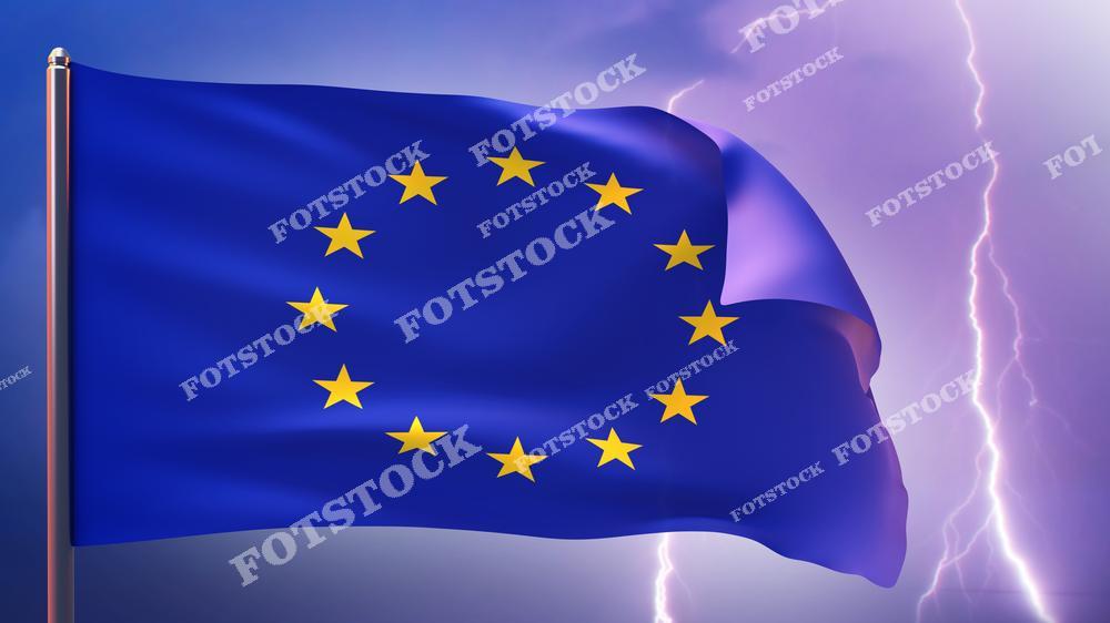 На изображении развевающийся флаг Европейского союза с двенадцатью звездами на фоне грозового неба и молний. Яркий свет молний создает драматическое ощущение. Фото ассоциируется с политическими и экономическими вызовами, стабильностью и изменениями.