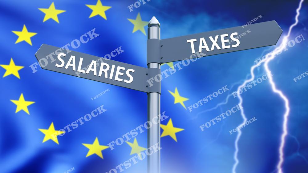 На изображении дорожный указатель с надписями "Salaries" и "Taxes", установленный на фоне флага Европейского Союза и грозового неба. Композиция иллюстрирует сложные экономические вопросы и напряжение в сфере налогообложения и доходов.
