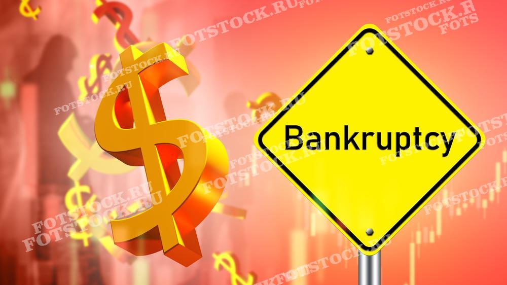 На фотографии изображены желтый знак с надписью "Bankruptcy" и золотой символ доллара на фоне красных финансовых графиков. Снимок символизирует финансовый кризис и банкротство, акцентируя внимание на экономической нестабильности и проблемах.