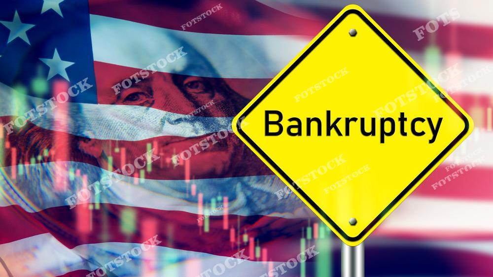На изображении жёлтый знак с надписью «Bankruptcy» на фоне флага США, наложенного на графики финансового рынка. Фото символизирует финансовые трудности, банкротства и экономическую нестабильность в Америке. Подходит для тем, связанных с кризисами, экономическими вызовами и падением бизнеса.
