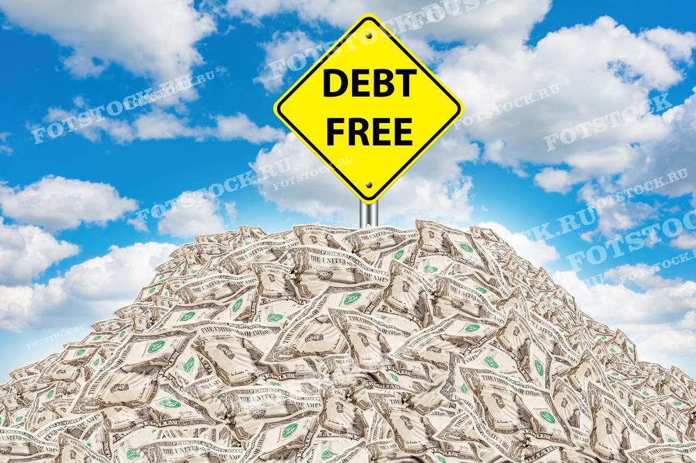 Фотография изображает дорожный знак с надписью "Debt Free" на вершине кучи долларов США. Сцена символизирует достижение финансовой свободы и отсутствие долгов. Голубое небо с облаками подчеркивает позитивный и свободный настрой. Изображение ассоциируется с успехом в финансовом планировании и управлении долгами.