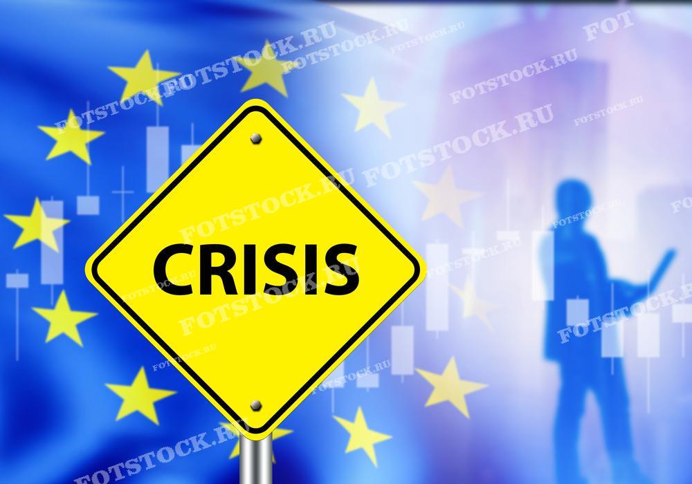 На изображении представлен желтый дорожный знак с надписью "Crisis" на фоне флага Европейского Союза. Этот знак символизирует экономический кризис и финансовые проблемы в странах Евросоюза. На фоне также видны графики и силуэт человека, что подчеркивает тему финансовых трудностей и нестабильности в экономике.