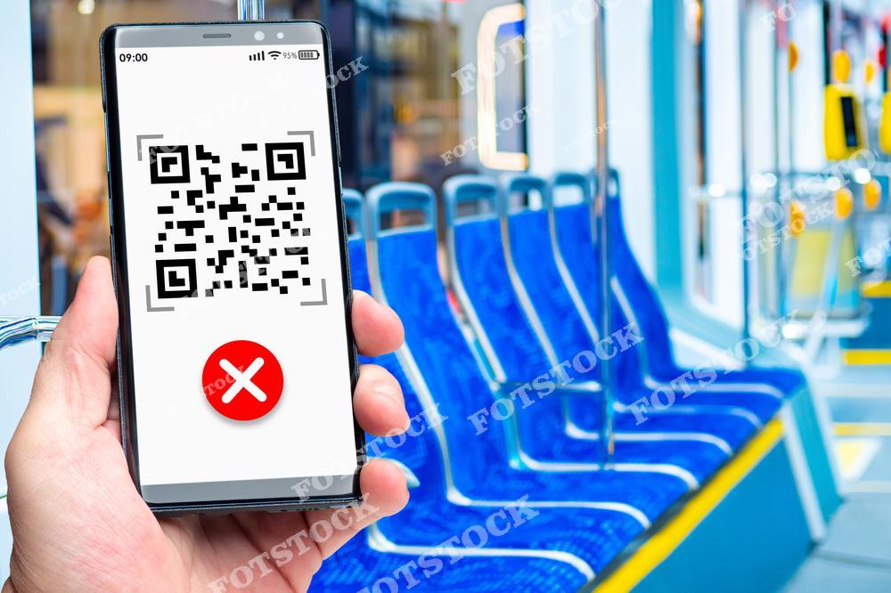 На изображении рука держит смартфон, на экране которого отображен QR-код с красным крестом, указывающим на ошибку или отказ в доступе. На заднем плане — пустые сиденья в общественном транспорте, что может символизировать проблему с оплатой проезда или сканированием билета. Фото иллюстрирует технологические сбои и их влияние на удобство передвижения.