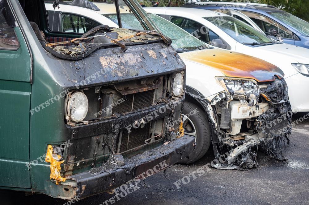 На переднем плане изображены два автомобиля, пострадавших в результате пожара. Видны обгоревшие элементы кузова, расплавленные детали и характерные следы огня. Снимок подчёркивает последствия возгорания и важность соблюдения пожарной безопасности в общественных местах.