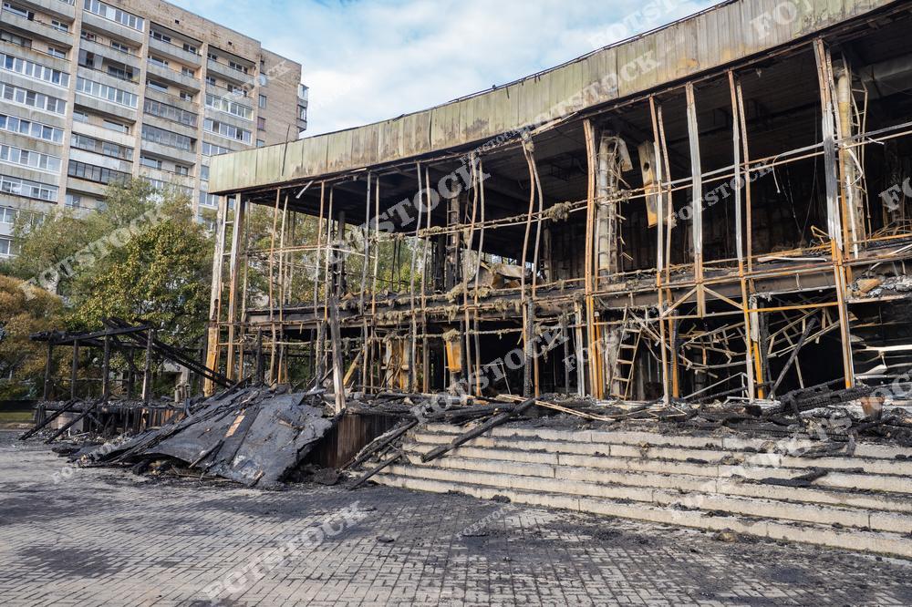 На фото показано разрушенное здание после крупного пожара. Каркас сооружения обгорел, стены отсутствуют, а металлические конструкции деформированы от воздействия высоких температур. Перед зданием заметны обугленные ступени и тротуар с следами копоти.