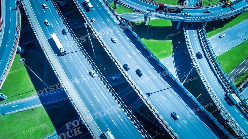 На фотографии изображена многополосная автомагистраль с перекрестком и развязкой. Снимок сделан с большой высоты, видно движение автомобилей в различных направлениях. Такое фото может использоваться для иллюстрации статей о дорожном движении, градостроительстве, планировке транспортной инфраструктуры, в учебных материалах по дорожному инженерингу или для декоративных целей. Оно также может быть полезным для исследователей и планировщиков городского развития, в брошюрах и рекламных материалах компаний, занимающихся производством автомобилей или дорожного оборудования.