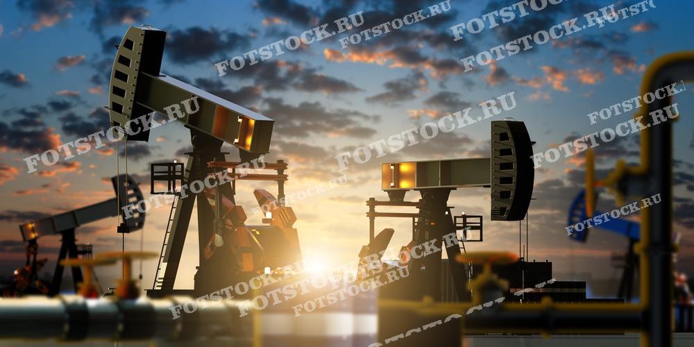 Фотография изображает несколько нефтяных качалок, работающих на нефтяном месторождении на фоне заката. Яркое освещение создаёт силуэтные изображения насосов, что подчёркивает атмосферность снимка. В кадре также видны элементы трубопроводной системы.