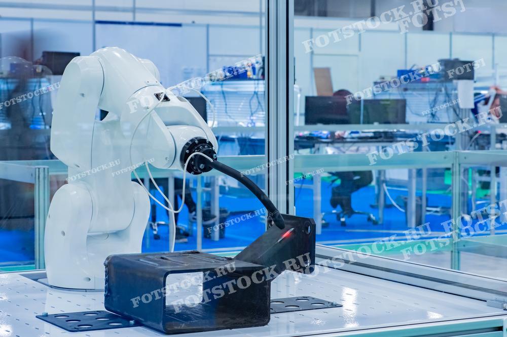 Фотография демонстрирует промышленного робота-манипулятора, работающего на производственной линии. Робот используется для выполнения различных задач по автоматизации производственных процессов. Виден внутренний интерьер производственного помещения с оборудованием и рабочими местами.