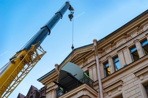 Фотография показывает процесс спуска больших предметов с использованием строительного лифта через балкон. Этот сюжет иллюстрирует технологические аспекты погрузочно-разгрузочных работ при строительстве или переезде. Образ на фотографии ассоциируется с организацией пространства внутри дома и использованием специализированной техники.

Фотография может быть использована для визуализации процессов грузоперевозок и строительных работ в рекламе или образовательных материалах, а также для документирования подобных событий.