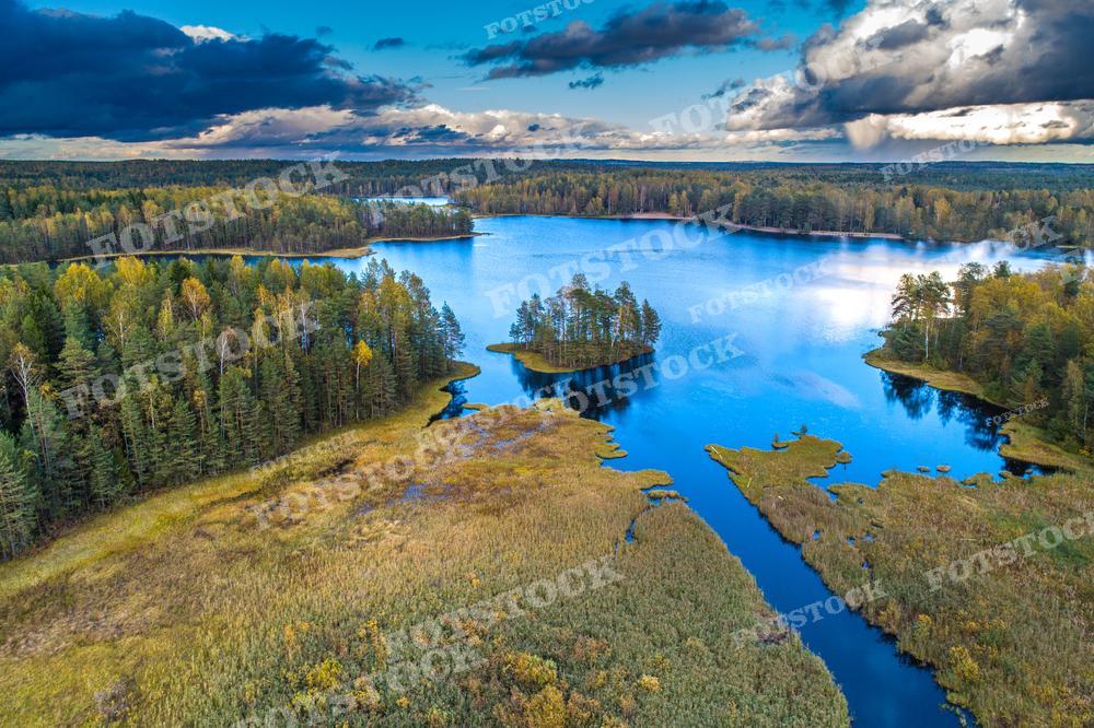 На фотографии с высоты птичьего полёта запечатлен осенний ландшафт, вероятно, Карелии. Мы видим лесной массив, озёра с островами и речные протоки. Над пейзажем нависают тёмные облака, предвещая изменение погоды. Эта фотография могла бы украсить статью о природном разнообразии, использоваться в научных работах о лесах или как визуальный материал в туристическом путеводителе по Карелии.