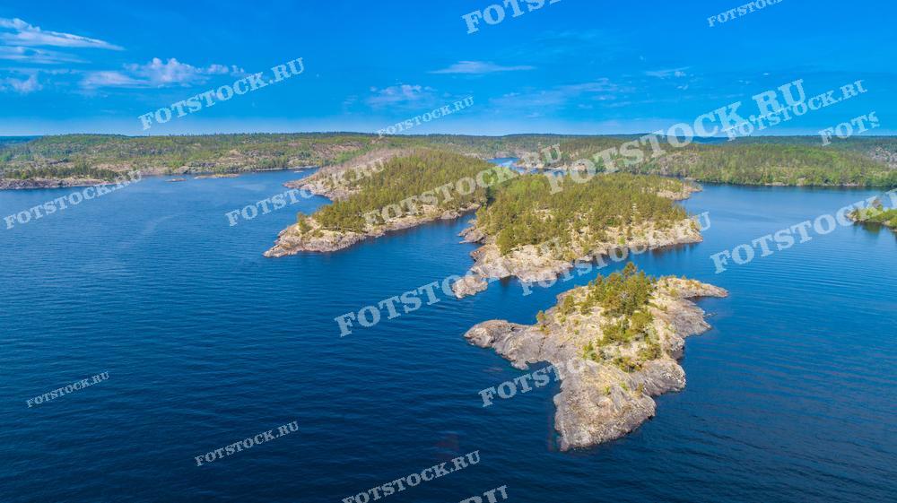 На фотографии изображены Ладожские шхеры — уникальные природные образования на Ладожском озере. Это один из самых красивых и популярных туристических маршрутов в Карелии, привлекающий своими скалистыми островами и чистыми водами. Ладожские шхеры славятся своими уникальными ландшафтами, в которых сочетаются скалы и зелёные леса. Данный вид снят с высоты, что позволяет полностью оценить красоту и масштабность этого места.