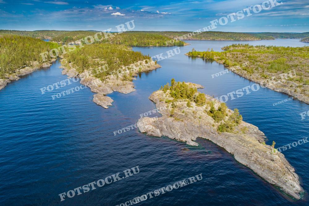 Фотография показывает Ладожские шхеры в Карелии, снятые с высоты. Виды на скалистые острова и зеленые леса создают неповторимую картину, отражающую природное великолепие этого региона. Ладожское озеро, самое большое в Европе, окружает эти острова, создавая впечатление покоя и умиротворенности. Это место является идеальным для отдыха на природе и привлечения туристов, ценящих живописные пейзажи.