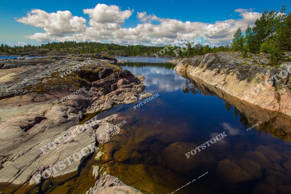 На фотографии запечатлены острова Ладожского озера с высоты, где каменистые шхеры создают величественный и уникальный пейзаж. Острова, окружённые прозрачной водой, словно утопают в зелени, а их скалистые берега подчёркивают дикость и первозданность природы Карелии. Это панорамное изображение Ладоги демонстрирует всю красоту и масштаб этого удивительного природного уголка России.