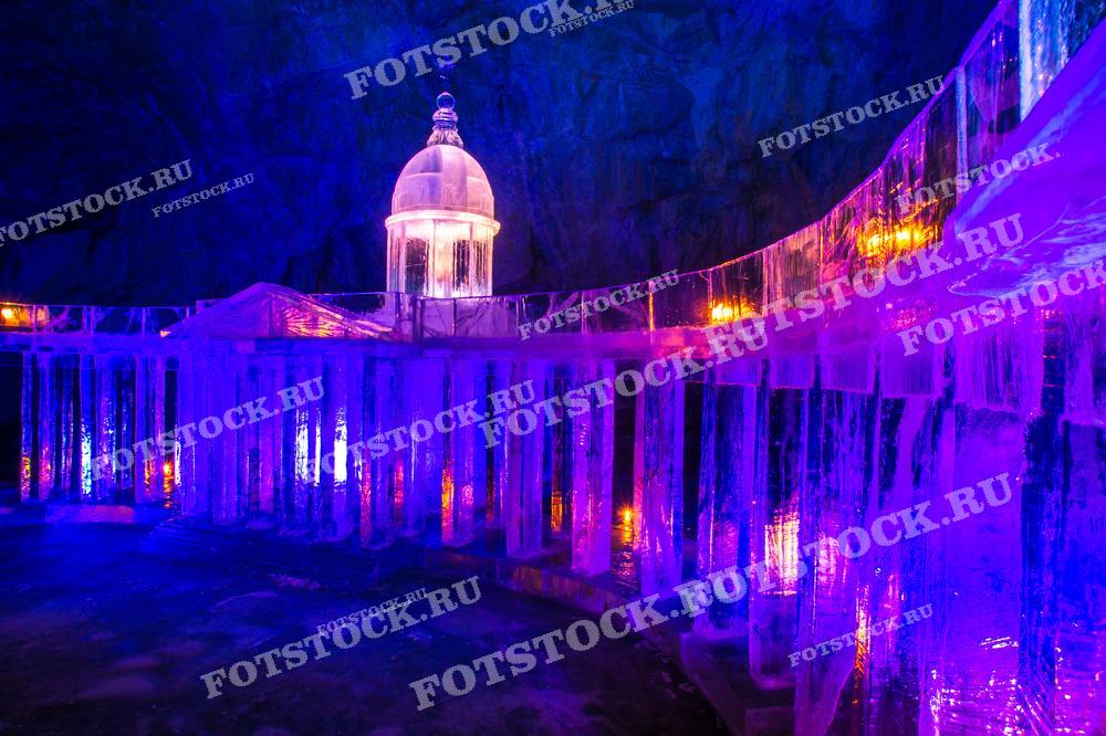 На фотографии изображен ледяной дворец, созданный в горном парке Рускеала в Карелии. Зимняя скульптура подсвечена разноцветными огнями, что подчеркивает структуру льда и создает волшебную атмосферу. Ледяные колонны и купол напоминают архитектурные элементы, выполненные изо льда.