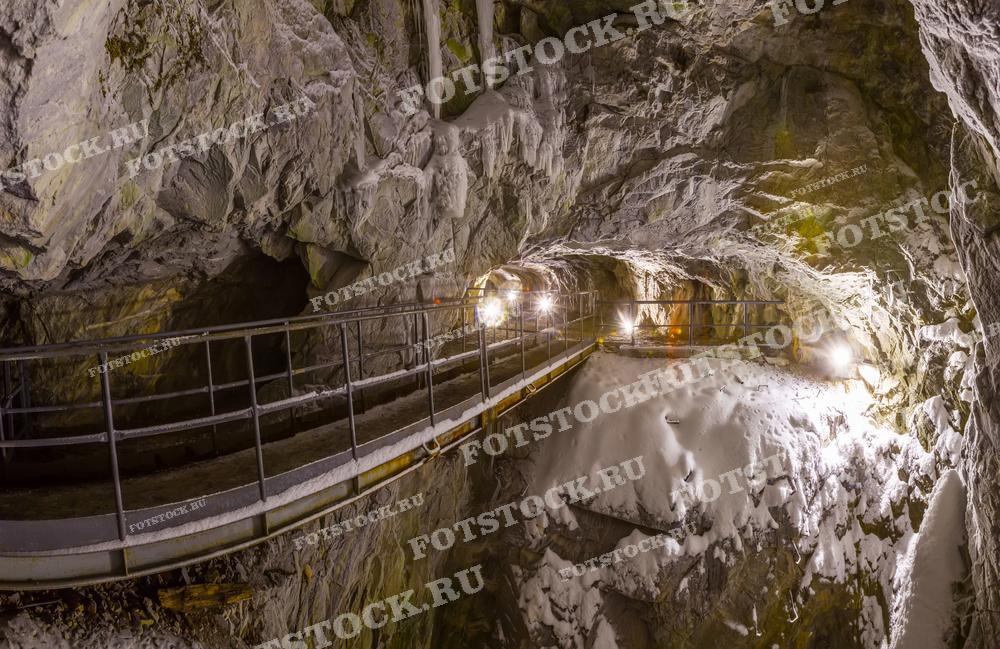 На фотографии изображен внутренний вид Рускеальского мраморного карьера в Карелии зимой. Путь ведет через снежные проходы, освещенные искусственным светом, который выделяет текстуру мраморных стен. Эта заснеженная, освещенная сцена создает мистическое и призрачное ощущение. Фотография идеально подходит для статей о необычных туристических местах России, геологии, а также может использоваться в материалах о приключенческом туризме.