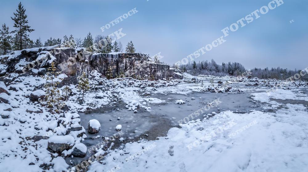 Фотография передает атмосферу зимней Карелии с ее заснеженными скалами и замерзшими водоемами. В кадре можно увидеть покрытые снегом деревья и величественные скальные породы, характерные для этого региона. Тишина и спокойствие этой зимней панорамы создают особую атмосферу уединения и гармонии. Карелия зимой привлекает туристов своей природной красотой, возможностями для зимнего отдыха и живописными пейзажами.