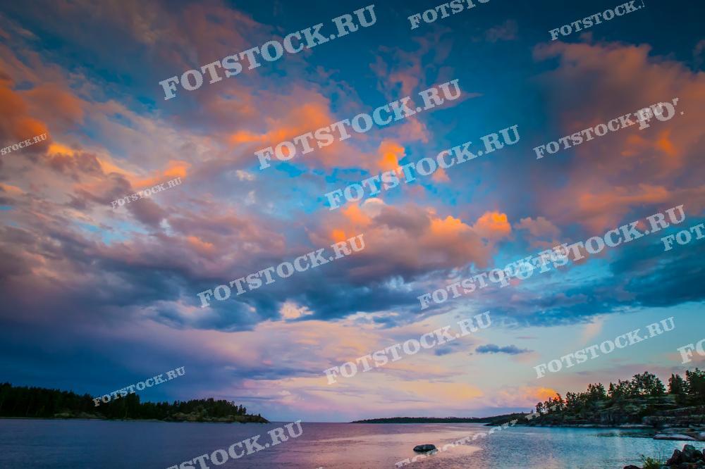 Фотография запечатлела закат над Ладожским озером в Карелии. Небо окрашено в розовые и оранжевые оттенки, создавая яркий и живописный пейзаж. Спокойная водная поверхность озера отражает краски закатного неба, усиливая эффект. Карелия славится своими красивыми закатами и уникальными природными видами, которые привлекают туристов со всего мира.