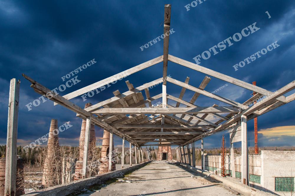 На фотографии изображён фрагмент заброшенного здания промышленного назначения на территории старого завода в Карелии. Остов крыши и бетонные опоры остались от конструкции, некогда служившей производственным или складским помещением. Вдали видны кирпичные трубы, типичные для бывших кирпичных или металлургических заводов. Подобные места встречаются в различных районах Карелии, включая Приозерск, Лахденпохью и окрестности Сортавалы, и представляют интерес для индустриального туризма и фотосъёмки.