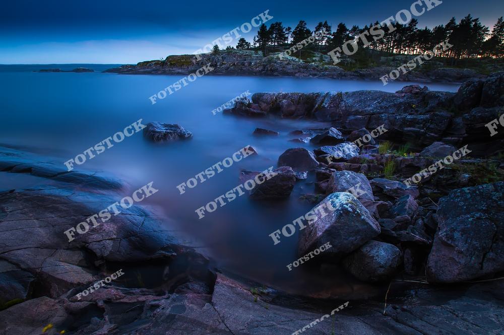 Фотография передает мистическую красоту Ладожских шхер в ночное время. Каменистый берег, поросший соснами, освещается последними лучами заката, создавая загадочную игру теней и света. Вода благодаря длительной экспозиции выглядит туманной и мягкой, добавляя снимку сюрреалистический эффект. Эти места привлекают путешественников, фотографов и романтиков, мечтающих о тишине и единении с природой.