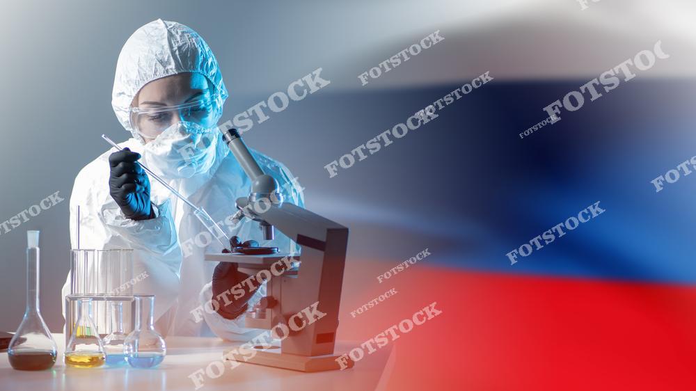 На изображении микробиолог в защитном костюме работает с биологическими препаратами в лаборатории. Он сидит перед микроскопом, что символизирует процесс научных исследований и разработки новых биологических препаратов в России. Фото подчеркивает важность исследований в области биотехнологий и биофармацевтики для развития медицинской науки и здравоохранения.