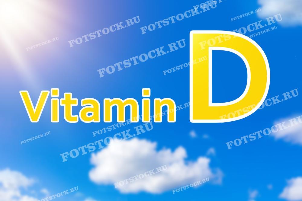 На изображении представлена надпись "Vitamin D" на фоне голубого неба с облаками и солнечным светом. Фотография символизирует важность солнечного света как естественного источника витамина D для поддержания здоровья.