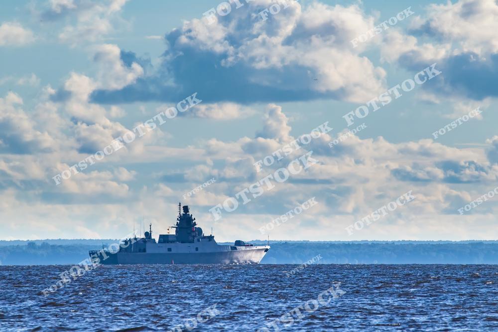 На фотографии изображен военный корабль, плывущий по спокойному морю под облачным небом. Судно находится на фоне горизонта, создавая ощущение масштабности и безмятежности. Морской пейзаж символизирует мощь и свободу.