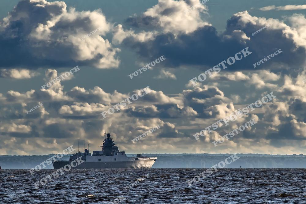 На фотографии изображён военный корабль, движущийся по морской глади под драматичным облачным небом. Корабль выделяется своей мощной конструкцией на фоне линии горизонта. Снимок символизирует мощь военно-морских сил и современное вооружение.