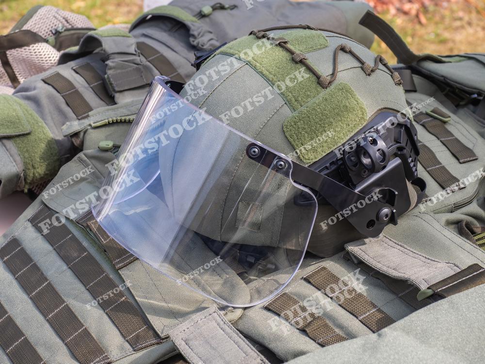 На фотографии изображен тактический шлем с защитным экраном, лежащий на бронежилете. Снаряжение демонстрирует современные технологии индивидуальной защиты. Кадр подчеркивает важность защиты и тактической готовности в полевых условиях.