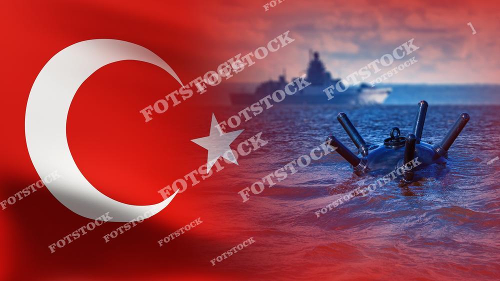 На изображении морская мина, находящаяся в водах у берегов Турции, с флагом Турции на заднем плане. Вдалеке виден гражданский корабль, плывущий рядом с опасной территорией. Фотография иллюстрирует риски для судоходства и стратегическое значение контроля морских границ.