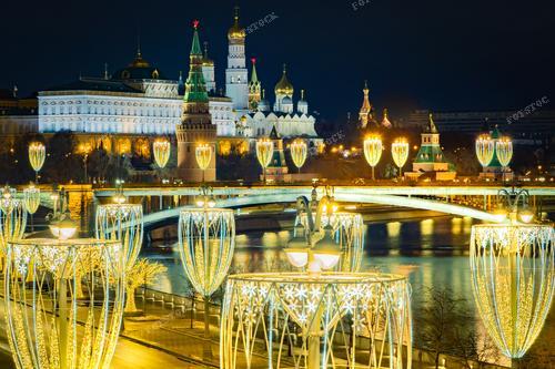 Вечерняя Москва, озаренная гирляндами и украшениями, воплощает в себе праздничное волшебство. Рождественские украшения, расположенные вдоль набережной Москвы-реки, создают неповторимую атмосферу праздника. 
Это фото передает уют и тепло встречи Нового года в российской столице. 
Изображение подходит для иллюстрации рождественских материалов, туристических путеводителей по Москве, а также для создания атмосферы в рекламе, связанной с новогодними праздниками.