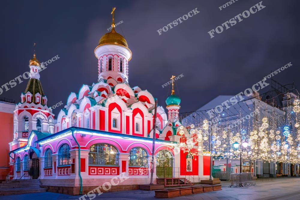 На фотографии изображен Казанский собор, расположенный на Красной площади в Москве. Яркие фасады храма гармонируют с новогодней иллюминацией на соседней Никольской улице. Собор выделяется своими золотыми куполами и красно-белой архитектурой, которая особенно эффектно смотрится в вечернее время. Праздничные огоньки на улице создают волшебную атмосферу, подчеркивая зимний праздничный дух столицы. Эта композиция передает сочетание истории и современных традиций празднования Нового года.