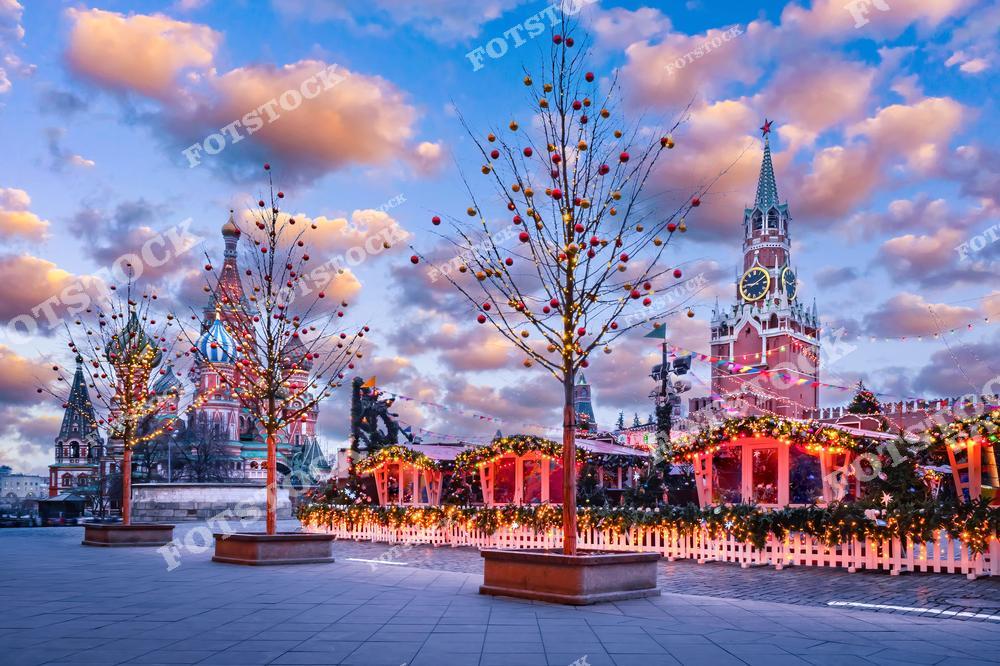 На фото изображена Красная площадь в Москве в новогоднюю ночь. В центре внимания – Собор Василия Блаженного с его яркими куполами, украшенный огнями. Вдоль площади стоят ёлки, украшенные гирляндами и яркими шарами, создавая атмосферу праздника. Вдалеке видна Спасская башня Кремля с часами, также подсвеченная огнями. Вся композиция наполнена рождественским духом и зимним волшебством, что делает эту сцену особенно красивой и атмосферной.
