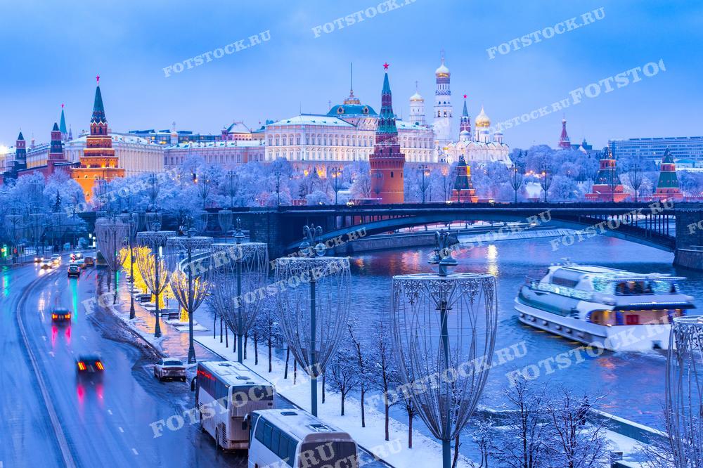 На фотографии изображен зимний вид на Москву-реку и Кремль в вечернее время. Заснеженные деревья и освещённые улицы добавляют магии зимнему городу. Речной трамвайчик, проходящий по Москве-реке, придает динамику сцене, а заснеженные купола Кремля и окружающих зданий создают ощущение праздничного настроения. Эта фотография идеально подходит для использования в туристических брошюрах, статьях о зимних праздниках в России или как украшение для рекламы зимних мероприятий.