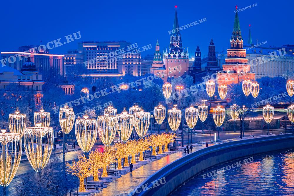 На фотографии изображена новогодняя иллюминация на набережной Москвы-реки с видом на Кремль. Светящиеся украшения и огни города создают праздничную атмосферу зимней Москвы. Фотография подходит для использования в материалах о новогодних праздниках, туристических буклетах и статьях о зимней Москве.