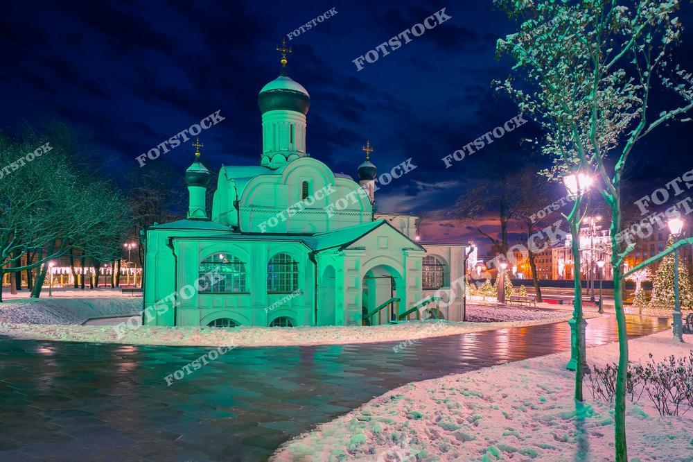На снимке запечатлён храм, расположенный в парке Зарядье. Здание освещено мягким светом, подчёркивающим его архитектурные детали. Вокруг лежит снежный покров, отражая свет уличных фонарей и праздничной иллюминации парка. Вдалеке виднеются огни современного города, создающие контраст с историческим храмом. Это место идеально передаёт спокойствие зимней Москвы и её гармонию между прошлым и настоящим.