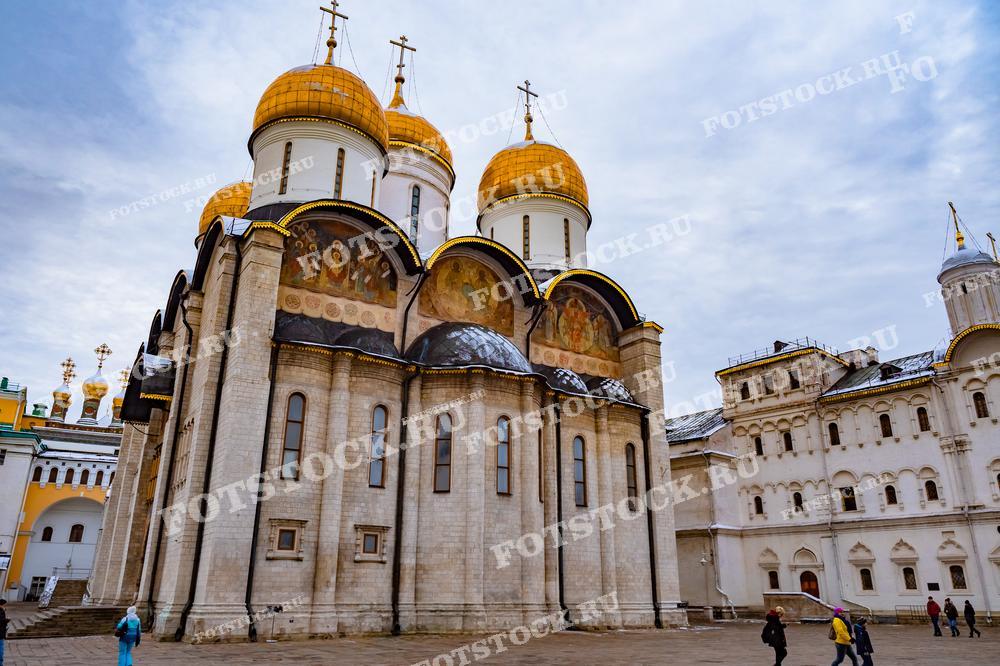 На фотографии изображен Успенский собор в Московском Кремле, один из главных православных храмов России. Его величественные золотые купола возвышаются над историческим центром Москвы. На переднем плане видны фрески и архитектурные детали, которые подчеркивают его историческое значение. Собор окружен другими кремлевскими постройками, создающими уникальный архитектурный ансамбль.