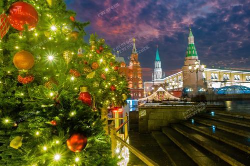 Фотография представляет собой зимний вечер в центре Москвы, где Рождественская ёлка величественно стоит рядом с Кремлем. Сияющие гирлянды и яркие шары создают атмосферу волшебства и тепла. Это идеальный снимок для использования в новогодних открытках, туристических рекламах и презентациях о российской зиме. Фотография иллюстрирует уникальную красоту Рождества и Нового года в столице России, делая ее отличным выбором для тех, кто ищет атмосферные иллюстрации к праздничным материалам.