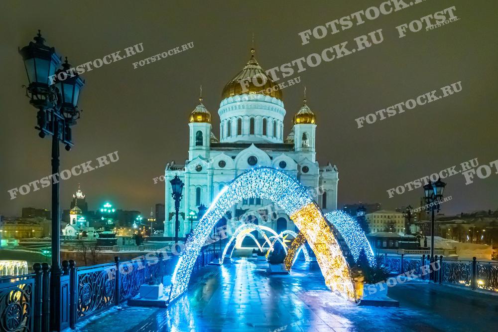 На фотографии изображен величественный Храм Христа Спасителя в Москве, освещённый ночными огнями. Перед храмом установлена арка из светящихся гирлянд, создающая праздничное настроение. Это место является популярным среди туристов и местных жителей, особенно в преддверии рождественских и новогодних праздников. Фотография может быть использована в туристических и культурных публикациях, подчеркивающих красоту Москвы зимой.